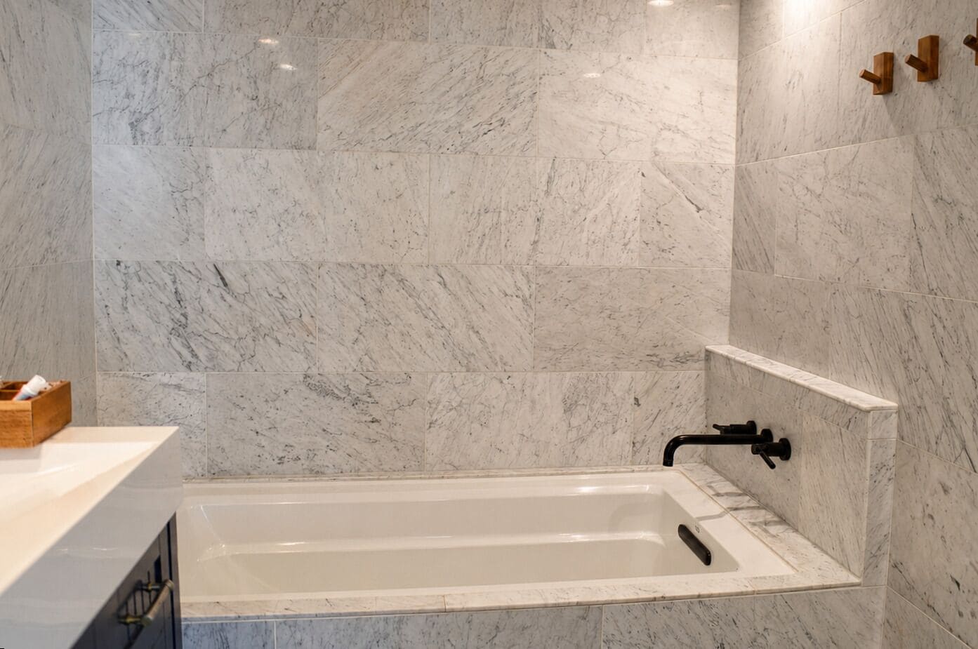 Un baño moderno con pared de mármol, una bañera blanca y una mesita de madera.