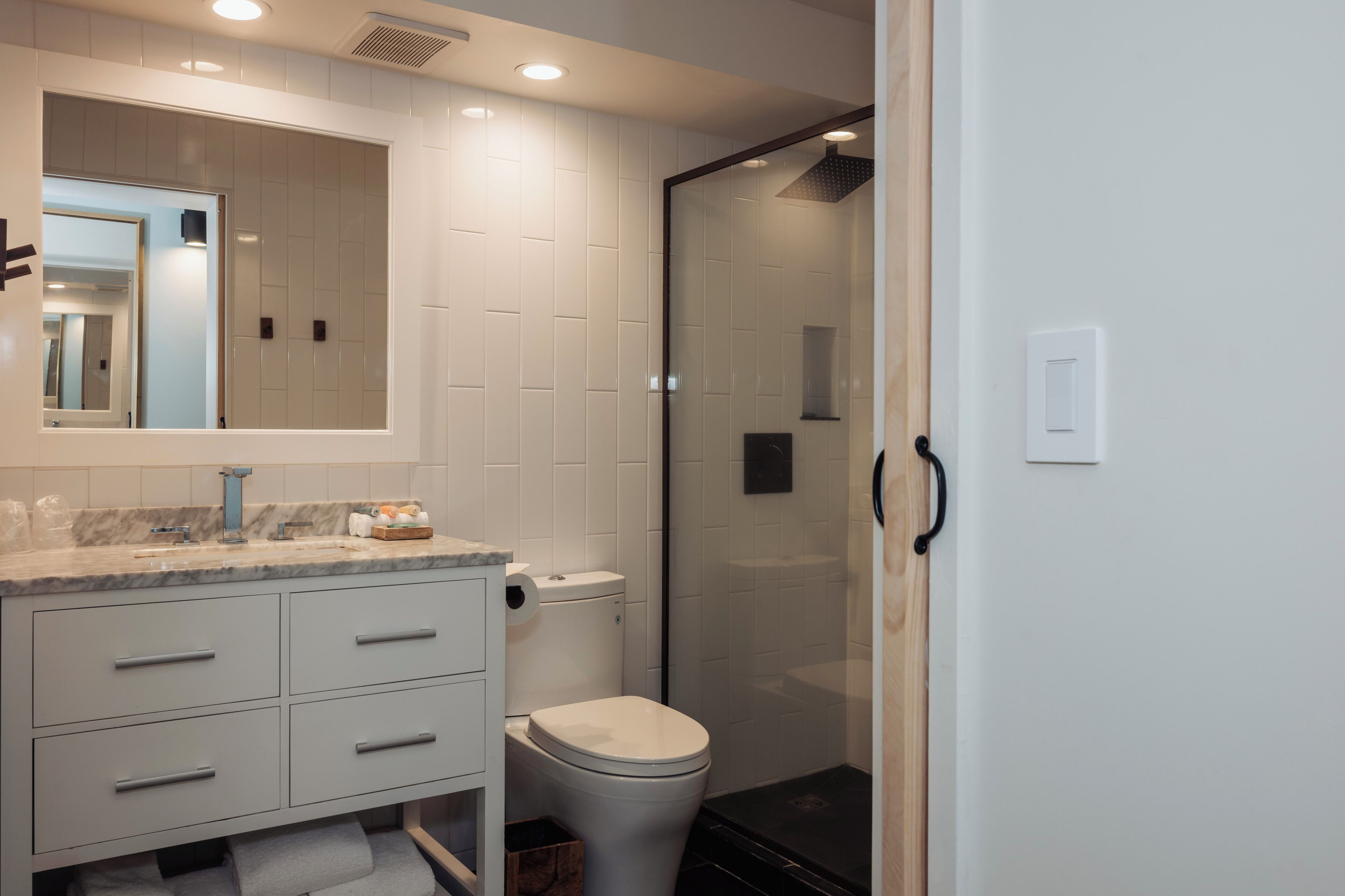 A modern bathroom with a marble countertop, a toilet, a glass-enclosed shower, and a large mirror.