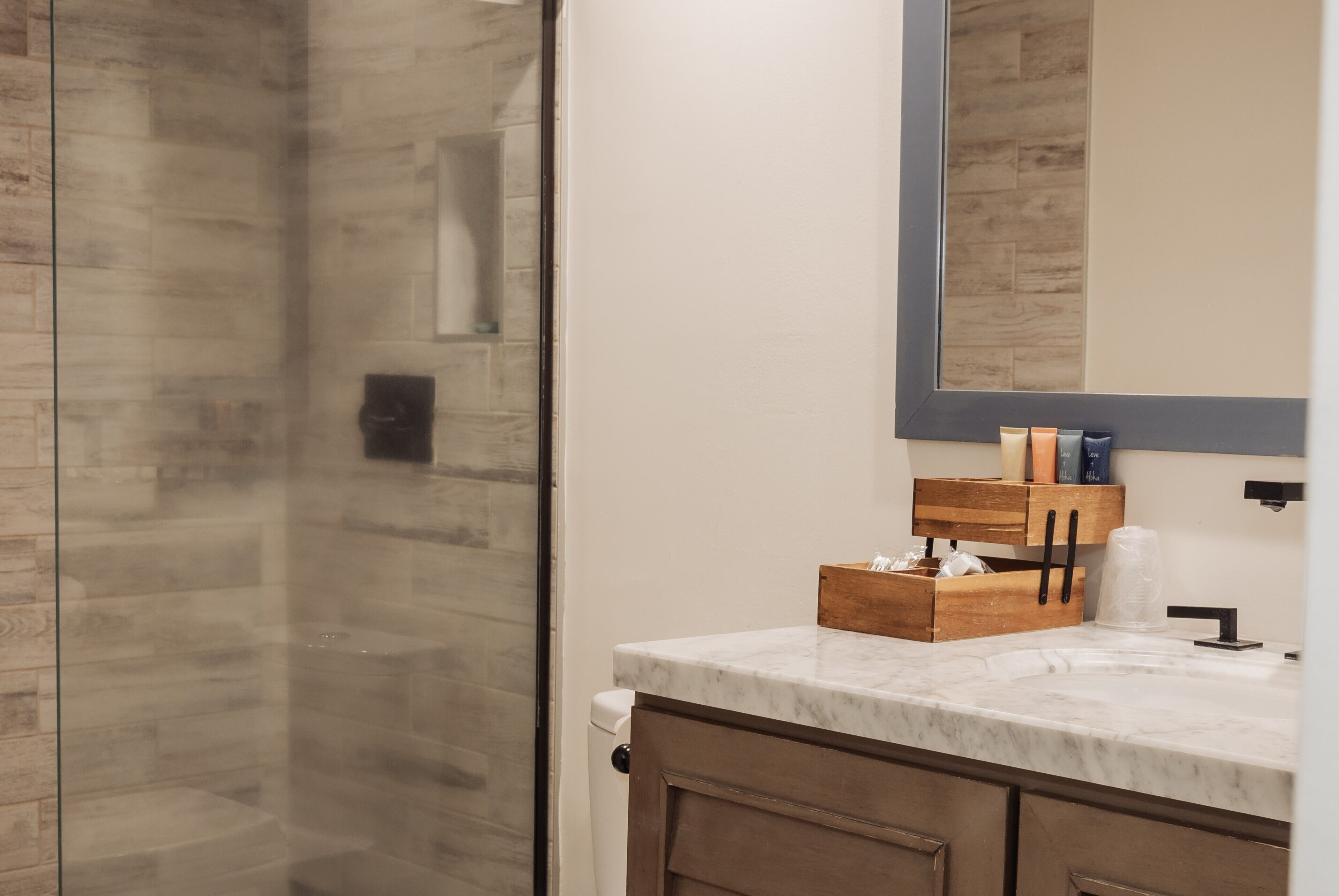 A bathroom with a glass shower enclosure, a marble countertop, and a wooden vanity with drawers.
