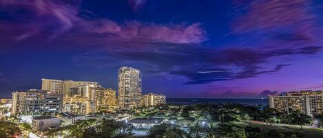 A nighttime cityscape with illuminated buildings and a clear view of the ocean.