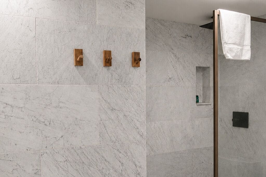 A bathroom with marble tiles, a wooden towel rack, and a glass shower enclosure.