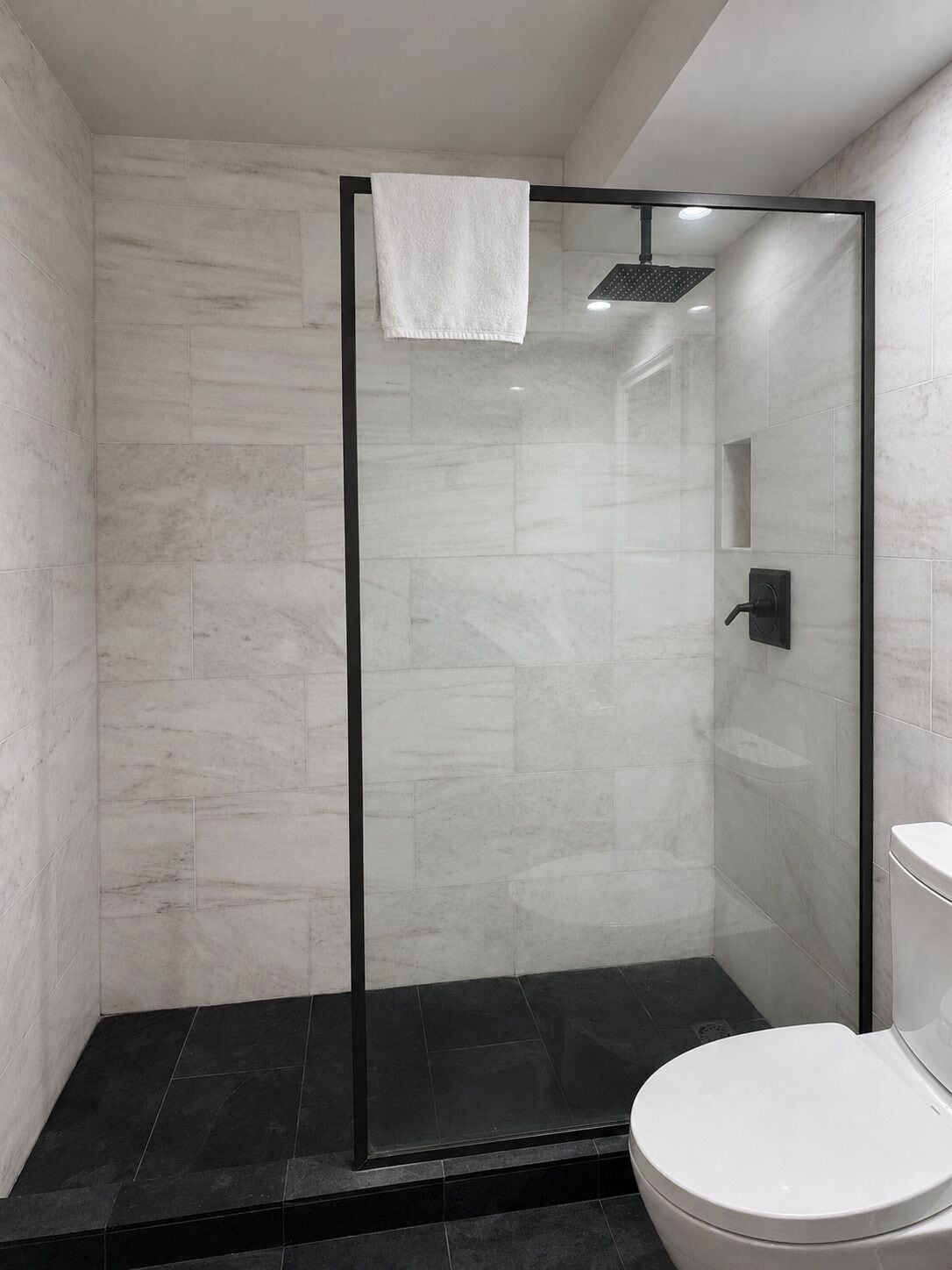 A modern bathroom with a glass-enclosed shower, a white toilet, and a marble-tiled wall.