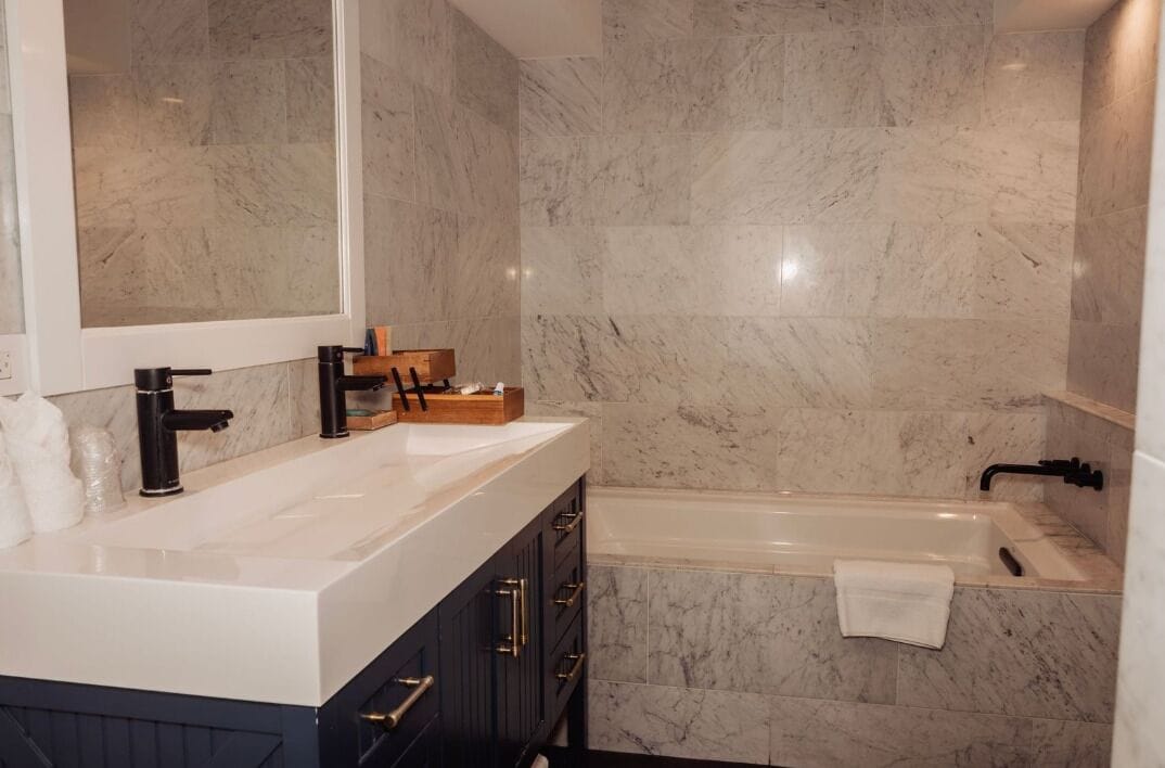 A modern bathroom with a marble sink, dark cabinetry, a large mirror, and a bathtub.