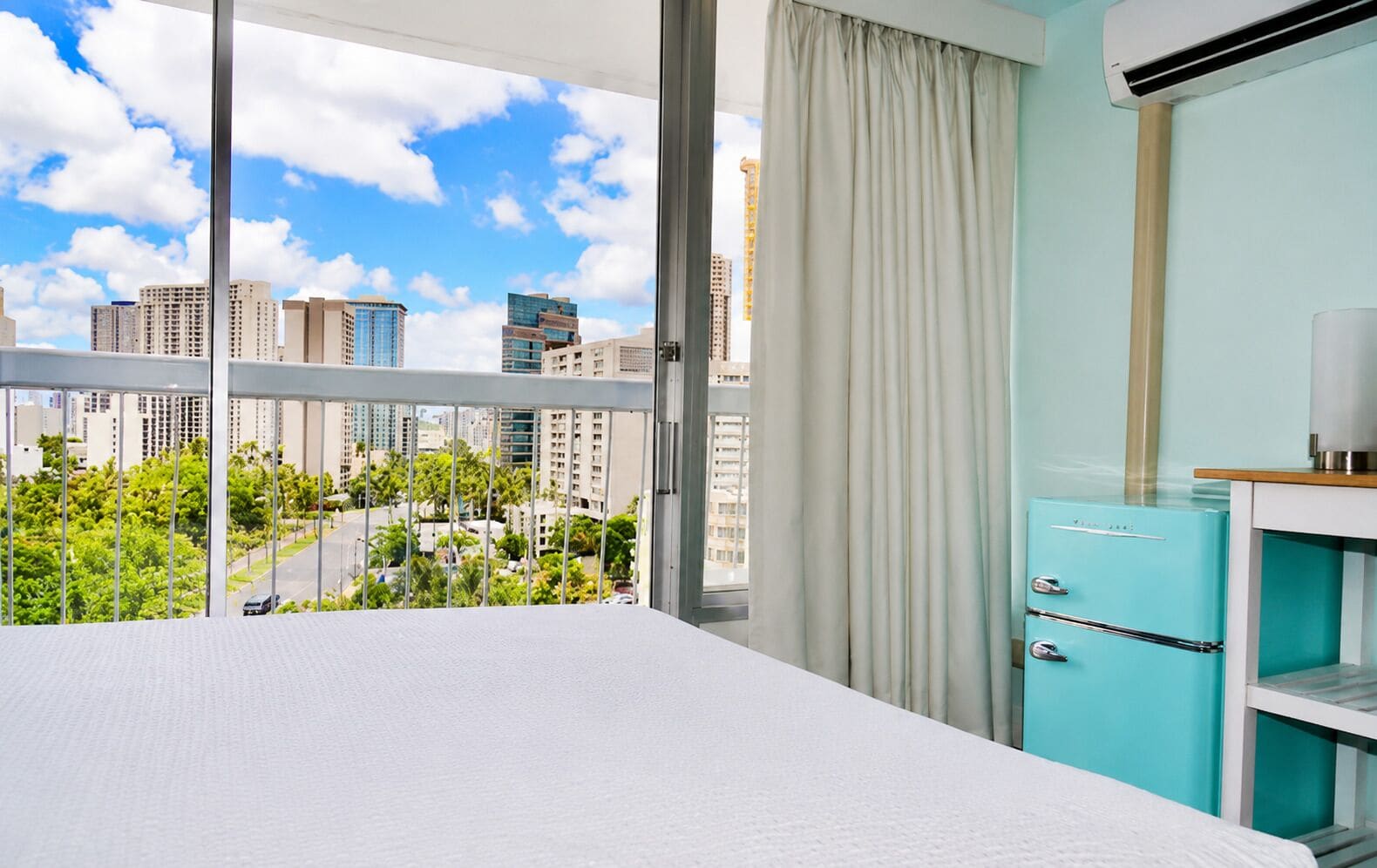 Habitación de hotel con balcón, vistas de la ciudad, kitchenette pequeña y una cama.