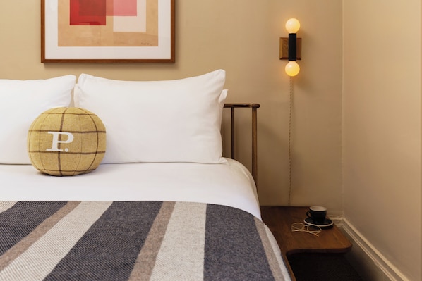 A neatly made bed with a striped bedspread, a pillow with a letter 'P', a framed artwork above the bed, and a bedside table with a lamp and a cup. - Palihotel San Francisco (San Francisco)