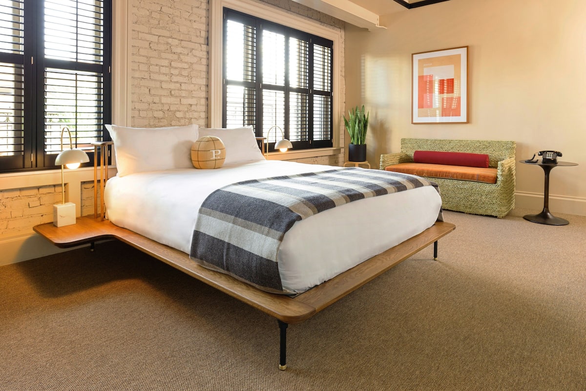 A modern hotel room with a large bed, a green sofa, a small table, and a potted plant.