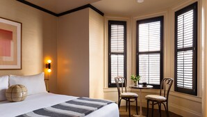 A hotel room with a large bed, a desk with two chairs, and a window with blinds.