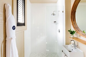 Bathroom features a white bathtub, sink, and mirror, with a potted plant and bathrobe nearby.
