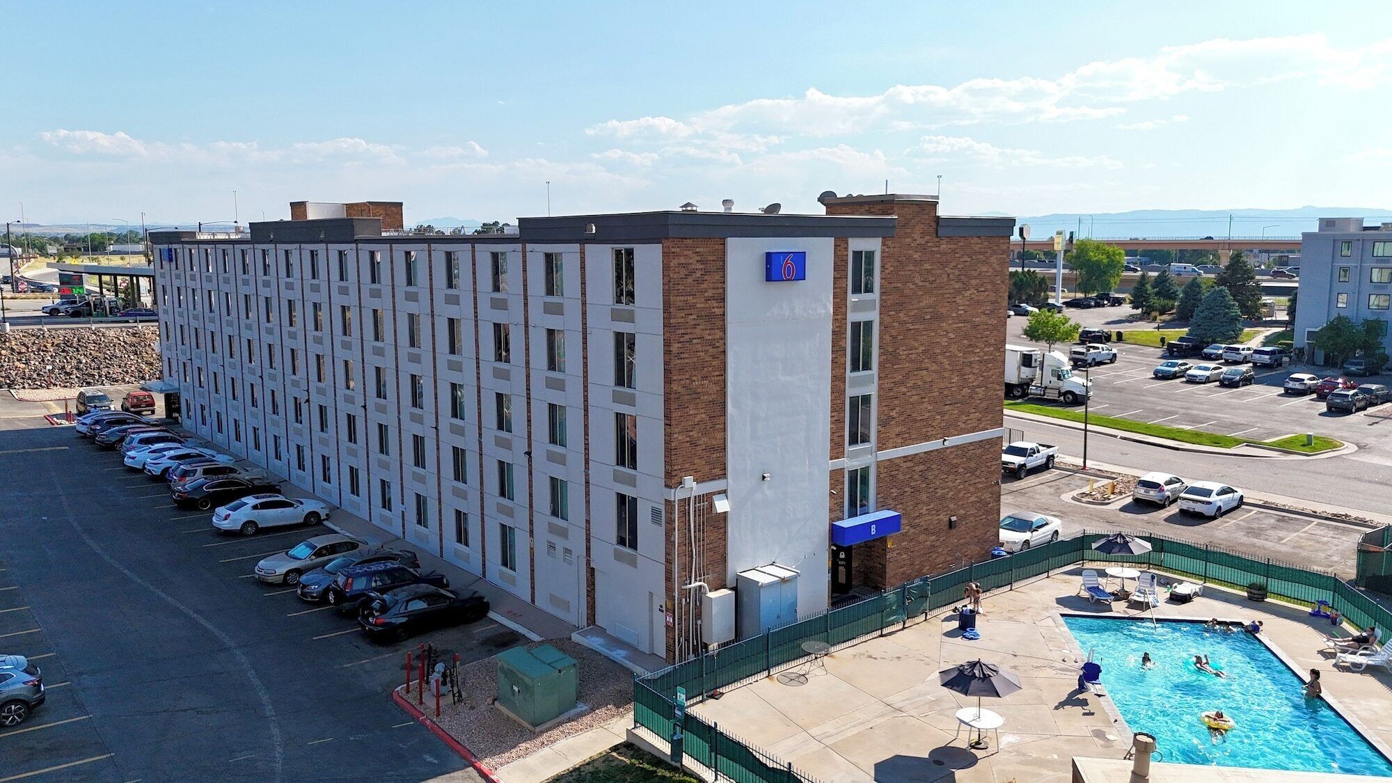 A multi-story hotel with a parking lot and a swimming pool.