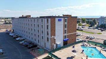 A multi-story hotel with a parking lot and a swimming pool.