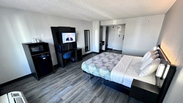Una habitación de hotel con cama, escritorio, televisión, microondas y refrigerador pequeño.