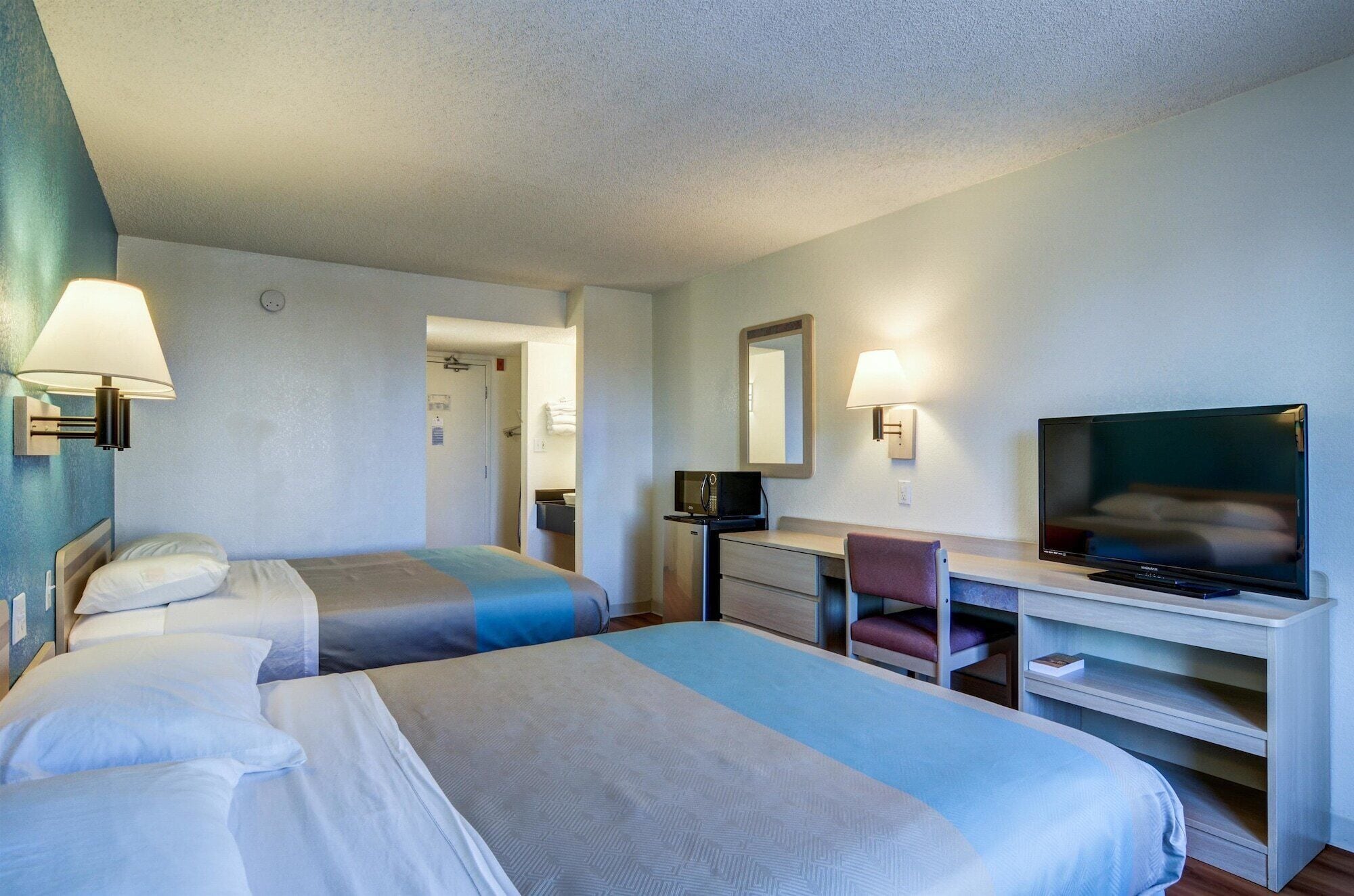 A hotel room with two beds, a desk, a chair, a television, and a mirror.