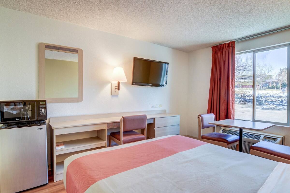 Ein Hotelzimmer mit Bett, Schreibtisch, Stuhl, Fernseher und einem Fenster mit Vorhängen.
