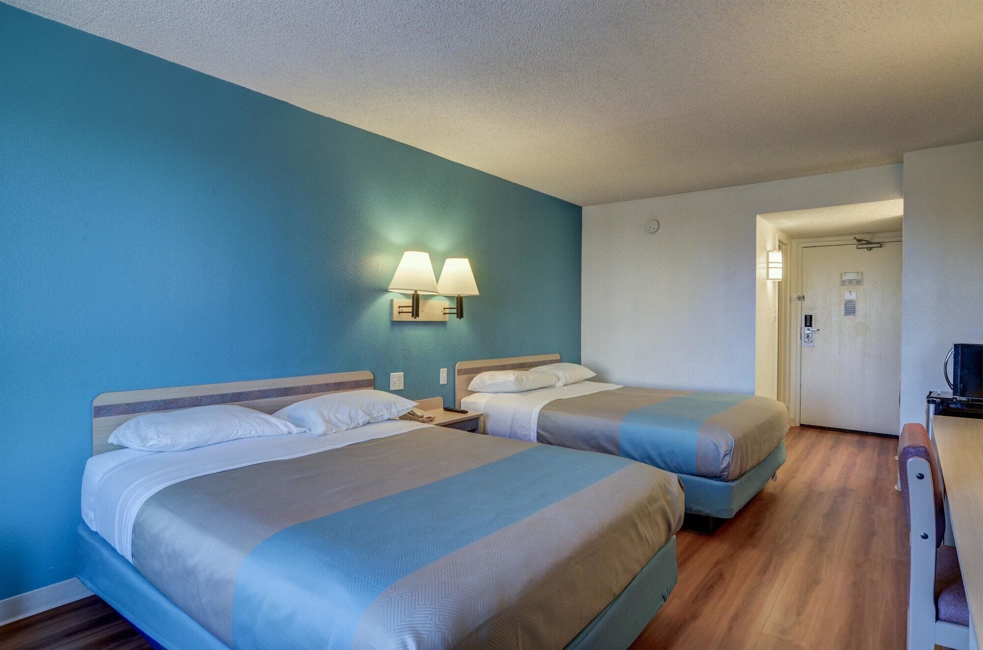 Habitación de hotel con dos camas, un escritorio y una puerta que da a otra habitación.