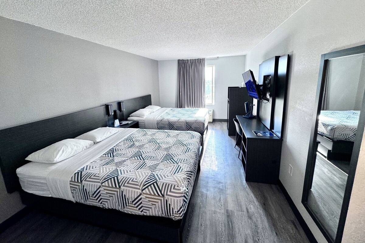 Ein Hotelzimmer mit zwei Betten, einem Schreibtisch mit Computer, einem Fernseher und einem großen Spiegel.