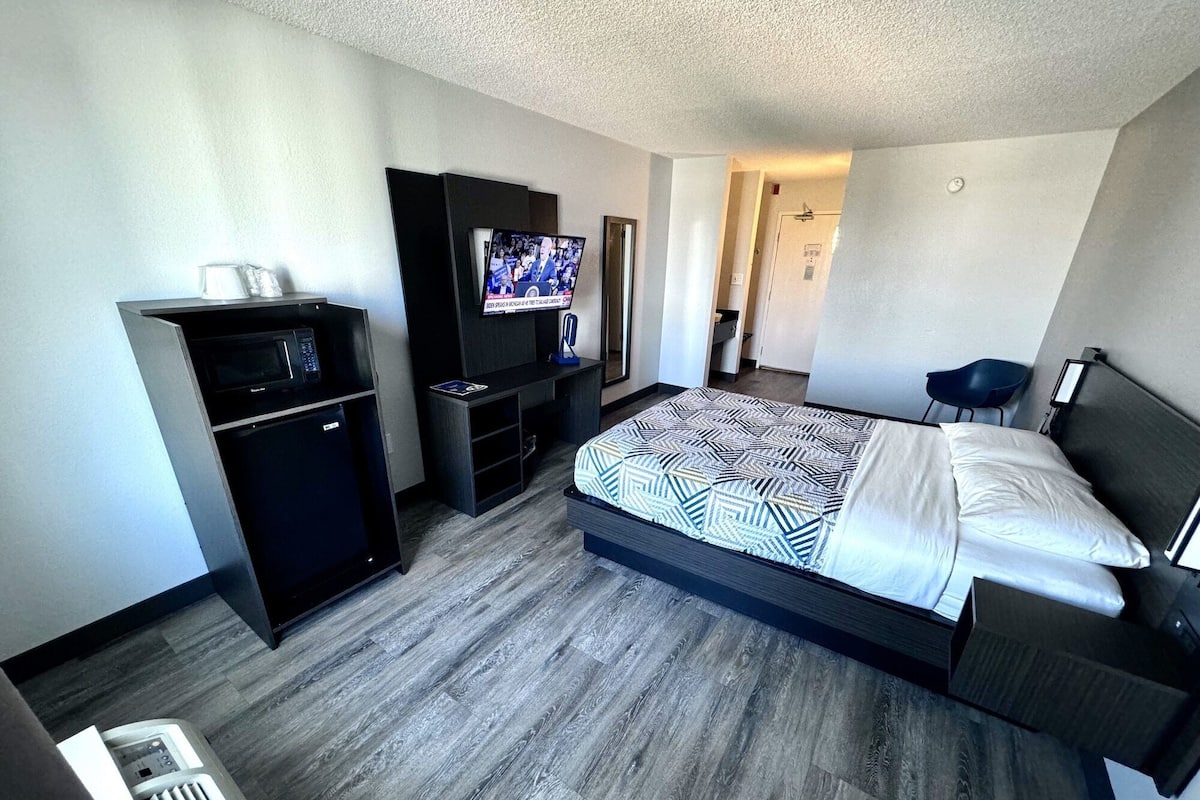 Ein modernes Hotelzimmer mit Bett, Fernseher, Minibar und einer Sitzecke.