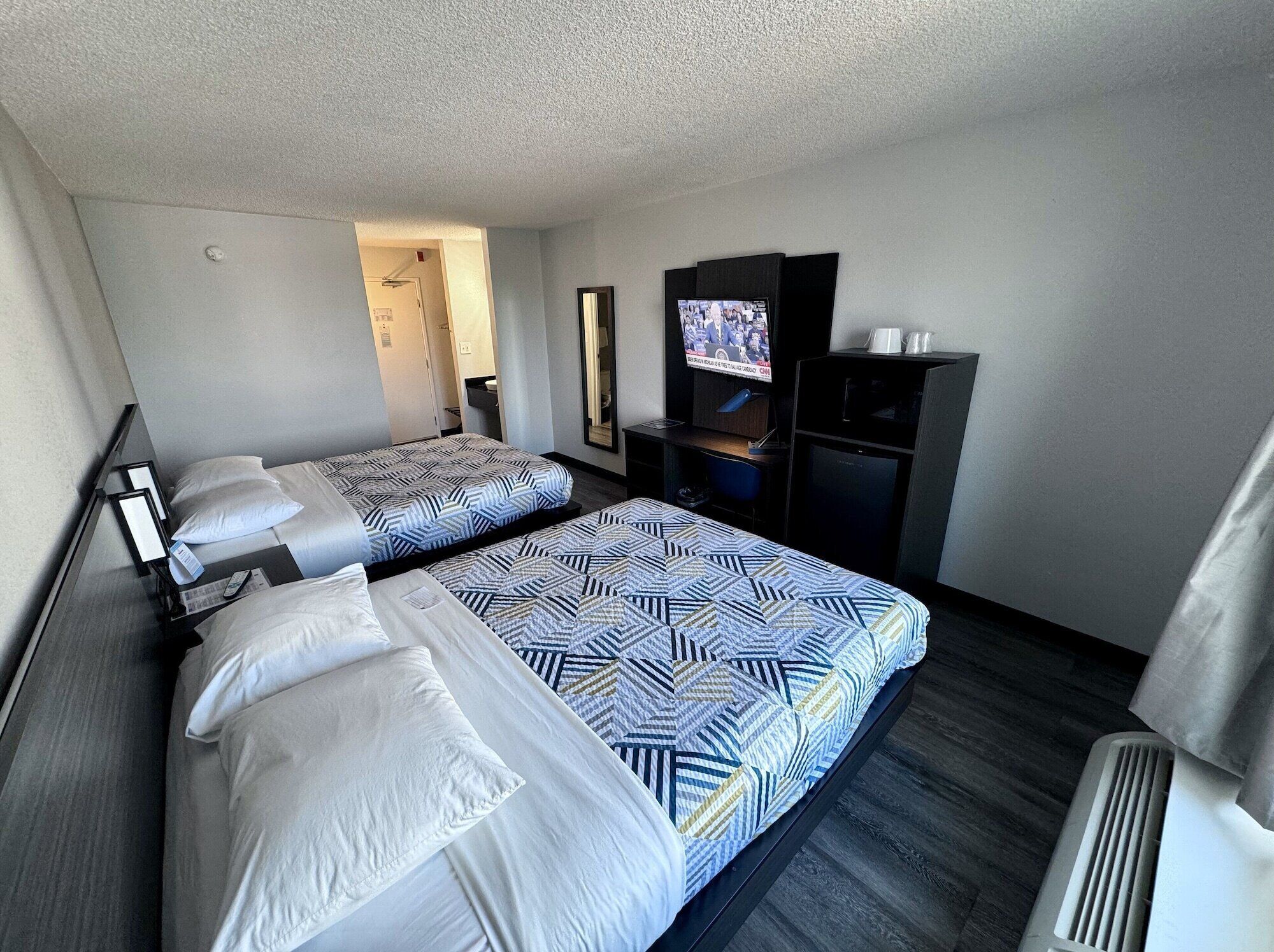 A hotel room with two beds, a TV, a desk, and a mirror.