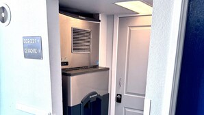 Máquina de hielo compacta con un letrero que indica su ubicación, una puerta y una rejilla de ventilación fijada a la pared.