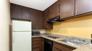 Una cocina con armarios de madera, un refrigerador blanco, microondas, lavavajillas y encimera de granito.