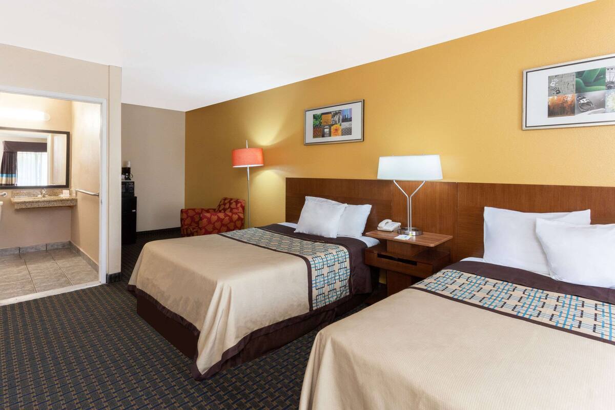 Habitación de hotel con dos camas, una mesita de noche, una lámpara, un teléfono y un cuadro en la pared.