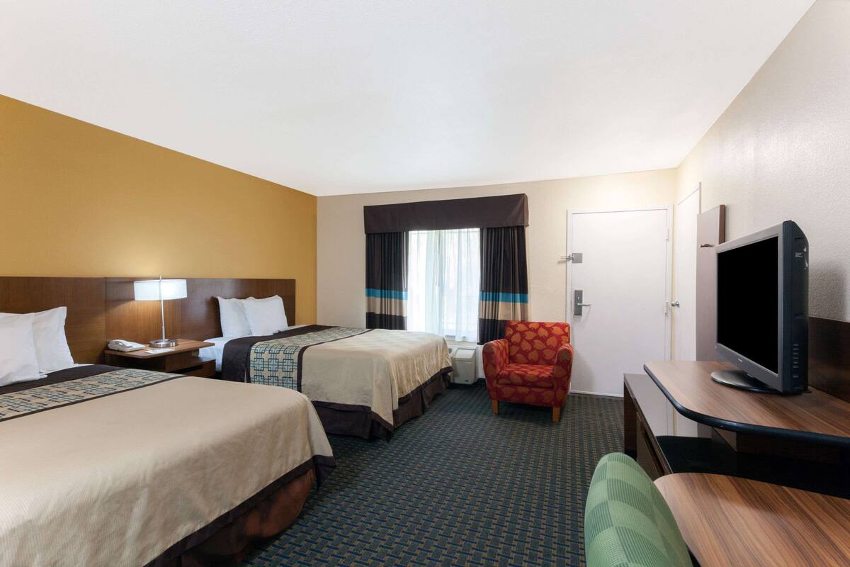 Una habitación de hotel con dos camas, televisión, escritorio y una silla.