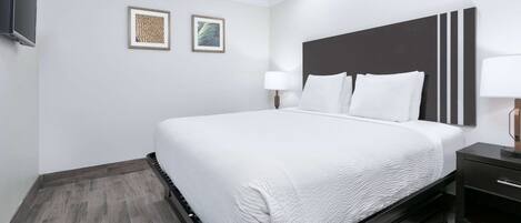 A modern hotel room with a large bed, a dark headboard, a bedside table with a lamp, and two framed pictures on the wall.