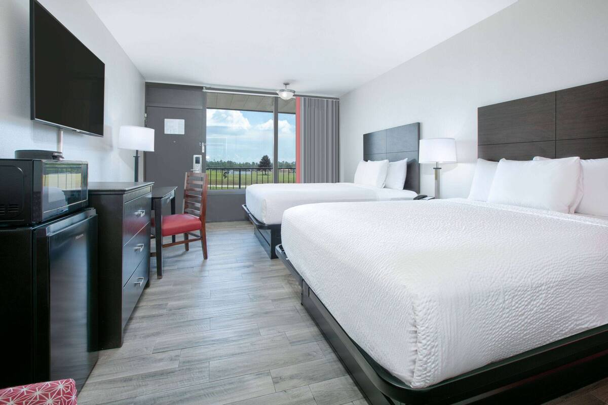 Habitación de hotel con cama, escritorio con televisor, silla y vistas al exterior.