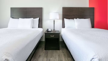 Habitación de hotel con dos camas, una mesita de noche con lámpara y una pared de acento roja.