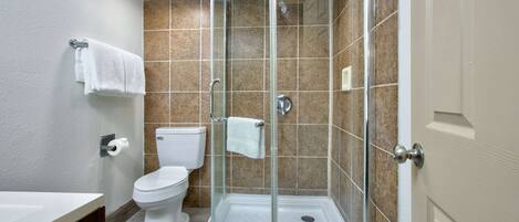 A modern bathroom with a glass-enclosed shower, a white toilet, and a sink with a wooden vanity.