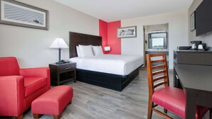 A hotel room with a bed, a desk, a chair, a red armchair, and a TV.