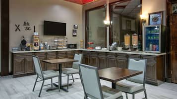 A modern restaurant interior with wooden cabinets, a large TV, and a counter with various food items.