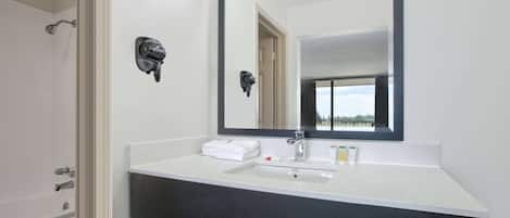 Une salle de bain avec un lavabo blanc, un plan de toilette foncé et un grand miroir.