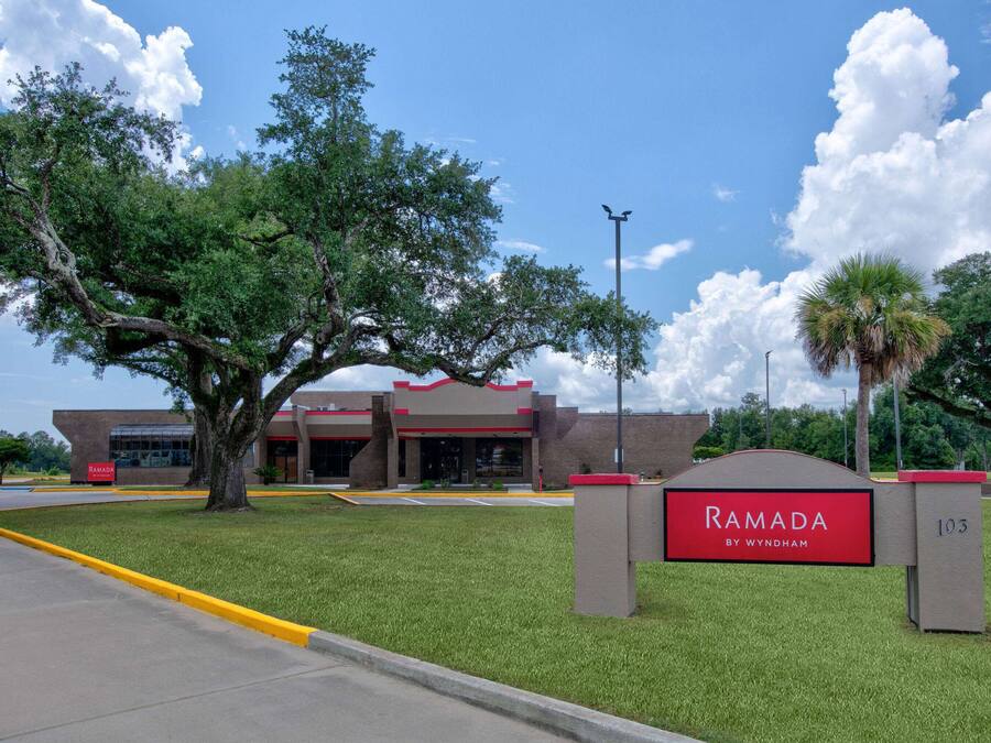 A hotel entrance with a sign reading "Ramada by Wyndham" and a large tree in the foreground.