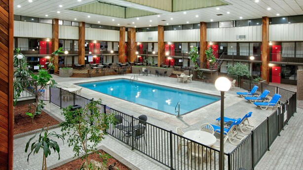 An indoor swimming pool with lounge chairs and tables, surrounded by wooden pillars and red lockers.