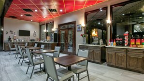 A restaurant with multiple tables and chairs, a kitchen area, and a counter with beverages.