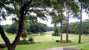 A golf course with a pond, trees, and a walking path.
