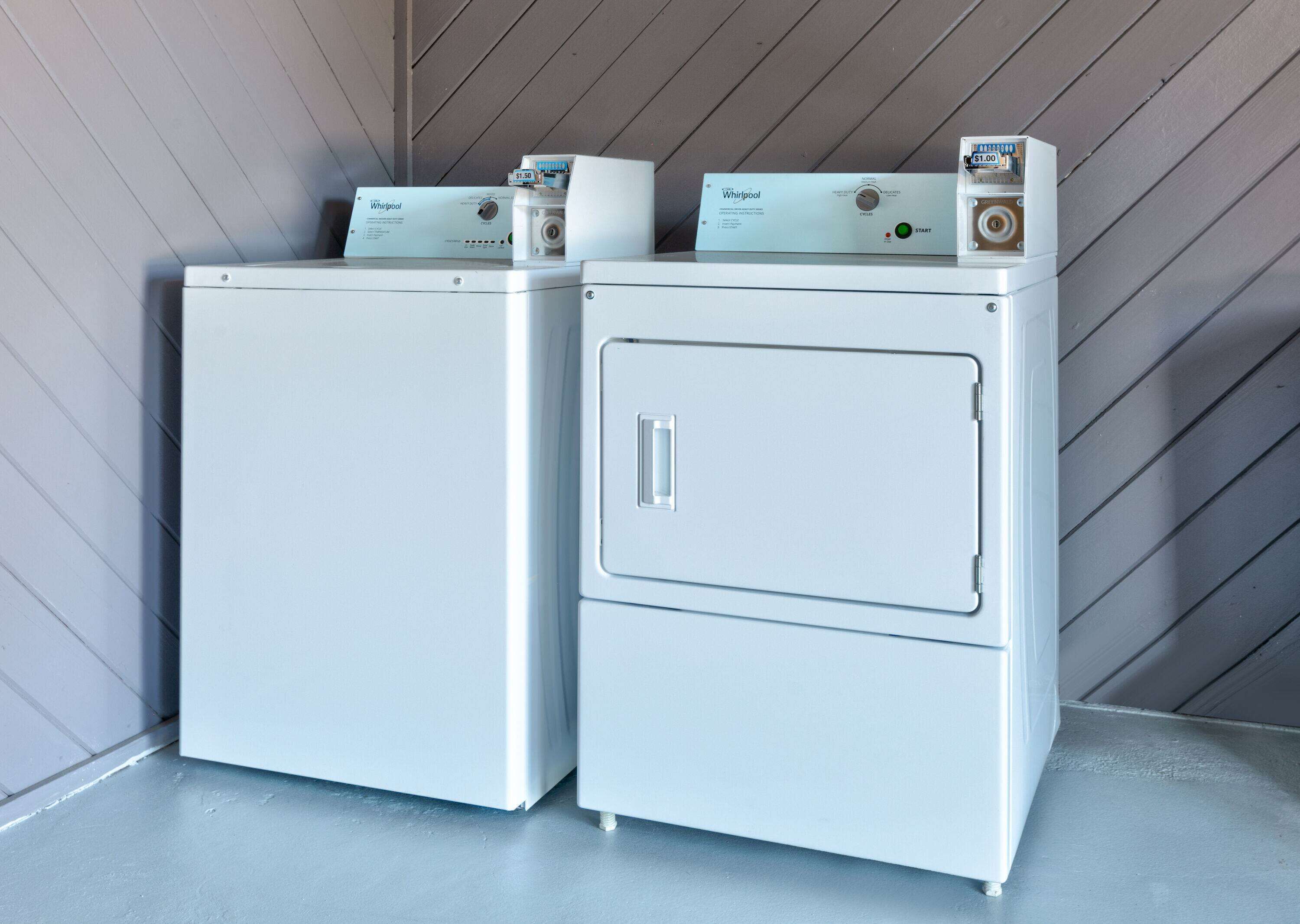 Twee gestapelde Whirlpool drogers in een wasruimte met een houten schuine plafond.