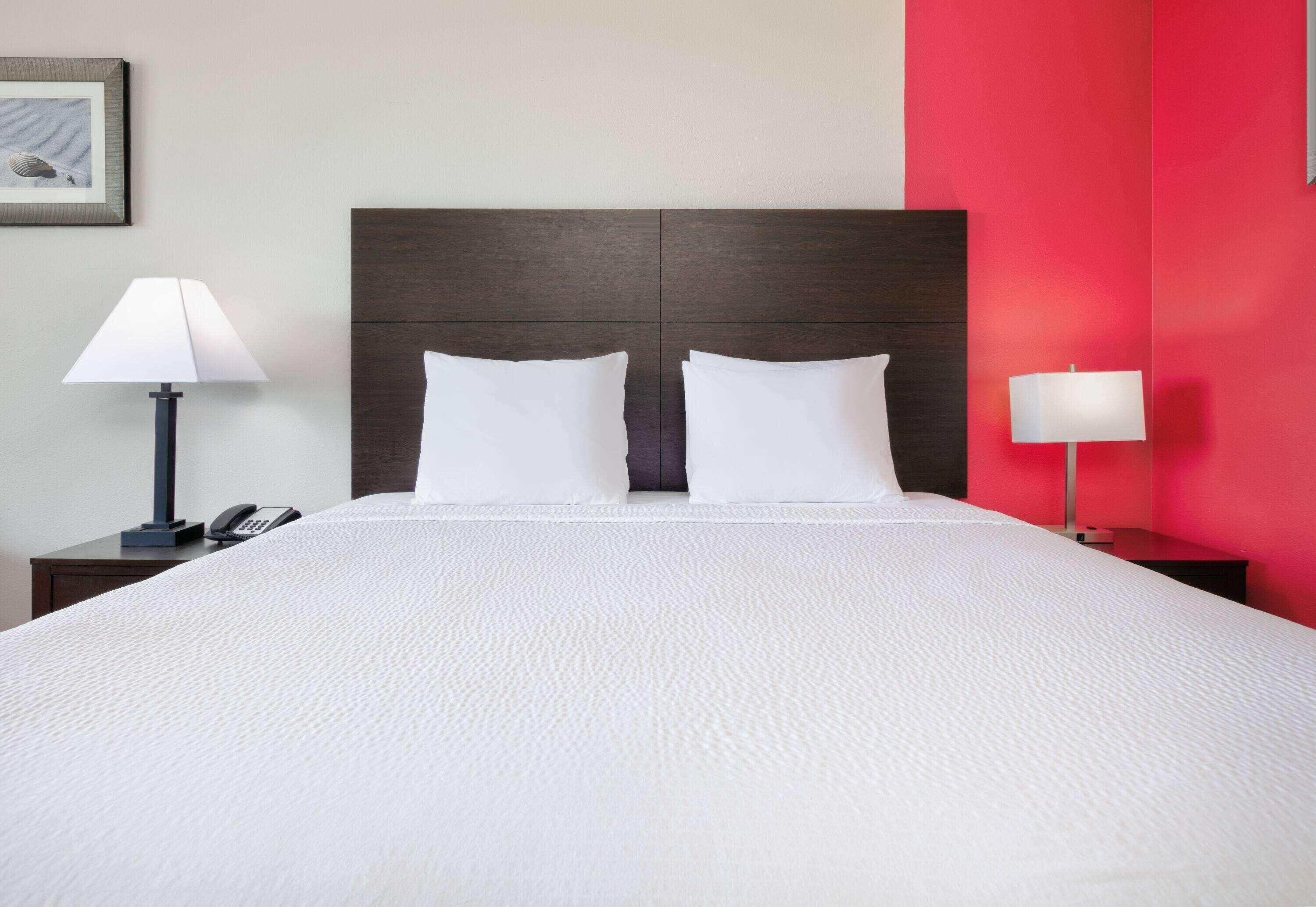 Un letto rifatto con cura, una testata scura, due comodini con lampade e una parete decorata di rosso.