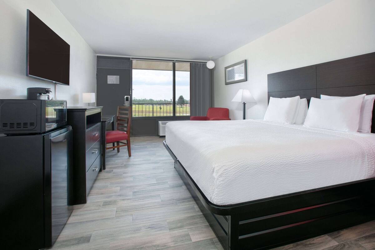 Habitación de hotel con cama, escritorio, silla y un amplio ventanal con vistas.