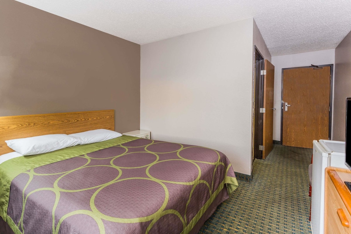 Una camera d'albergo con un letto, una testiera in legno, una coperta verde e viola, una televisione e una piccola scrivania con una sedia.