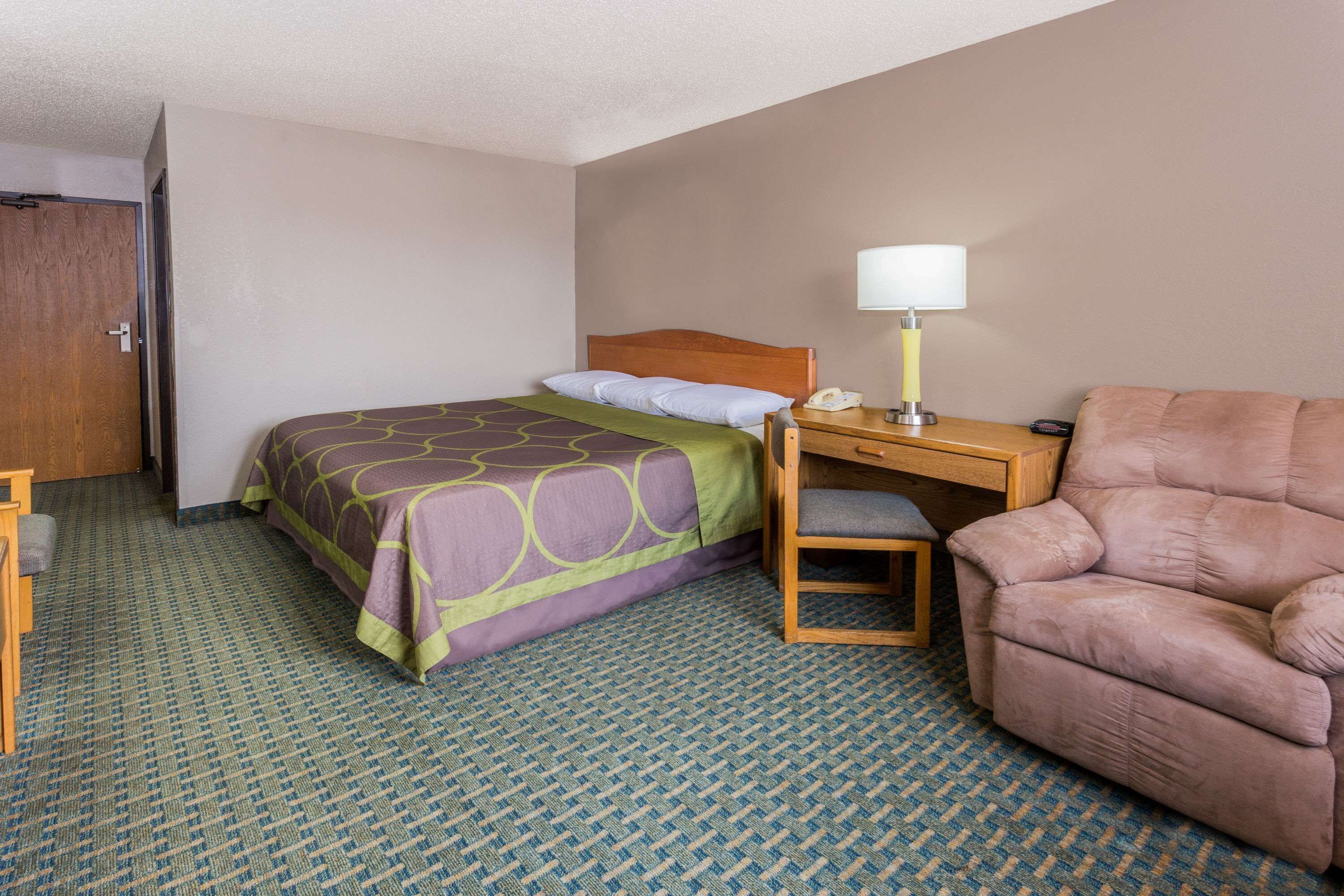 Une chambre d’hôtel avec un lit, un bureau avec une lampe, une chaise et une porte.