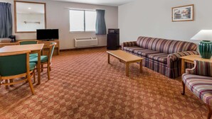 A hotel room with a dining area, a sofa set, a television, and a window with curtains. - Super 8 by Wyndham St. Charles (St. Charles)