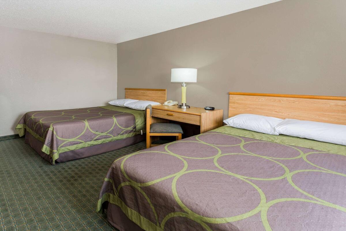 A hotel room with two beds, a desk, a lamp, and a chair.