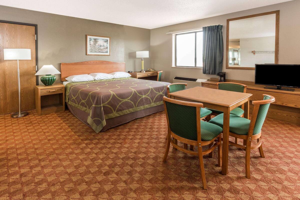 A hotel room with a bed, a desk, a chair, a television, and a window with curtains.