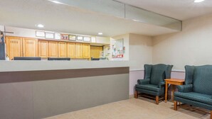 A reception area with a counter, wooden cabinets, and two green armchairs. - Super 8 by Wyndham St. Charles (St. Charles)
