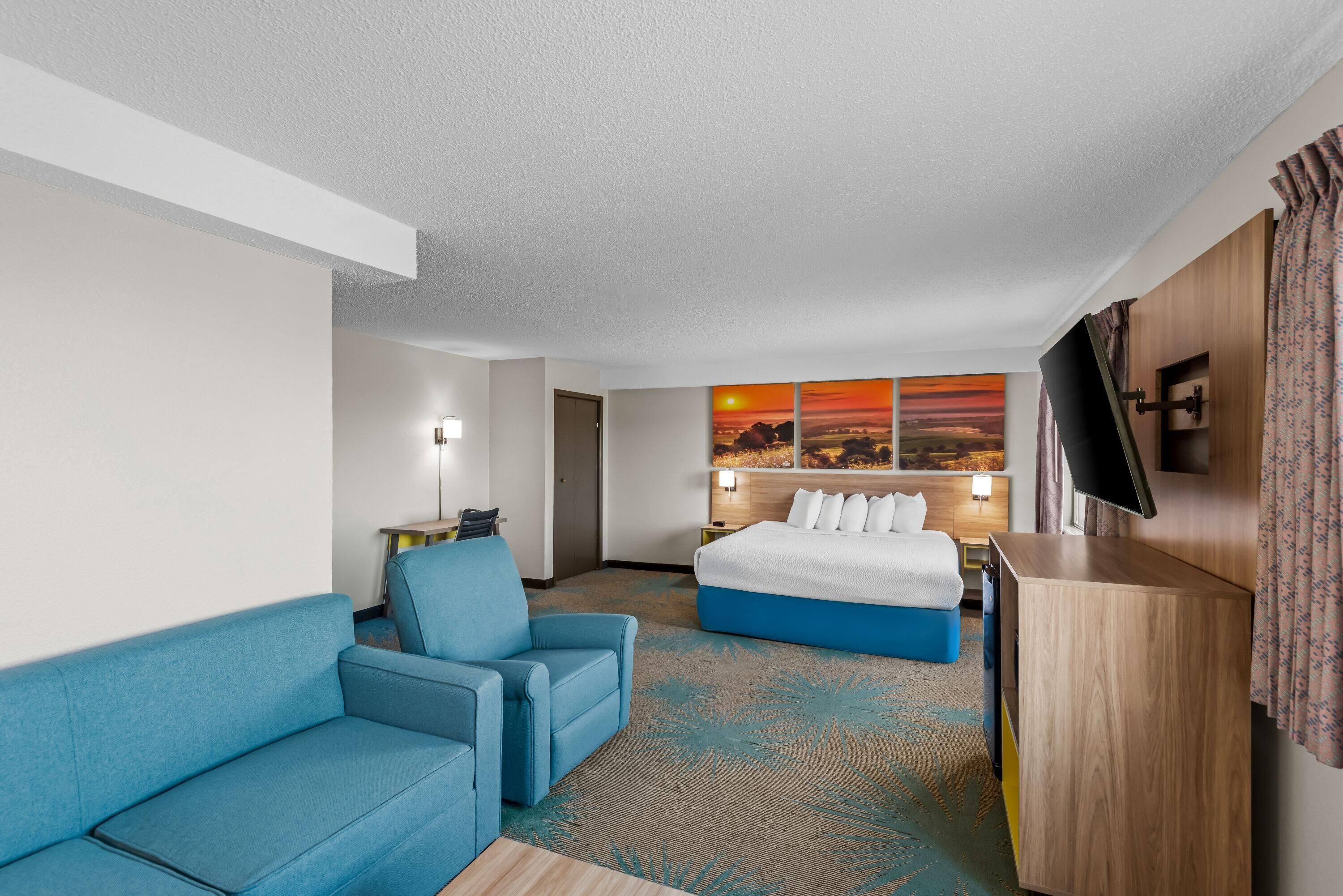 Une chambre d’hôtel avec un lit, un canapé bleu, un téléviseur à écran plat et un tableau représentant un coucher de soleil.