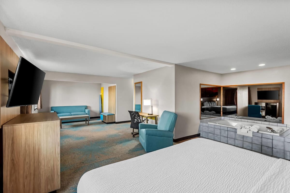 Une chambre d’hôtel comprenant un lit, un bureau, une chaise, une télévision, un canapé et une salle de bain avec une baignoire et un miroir.