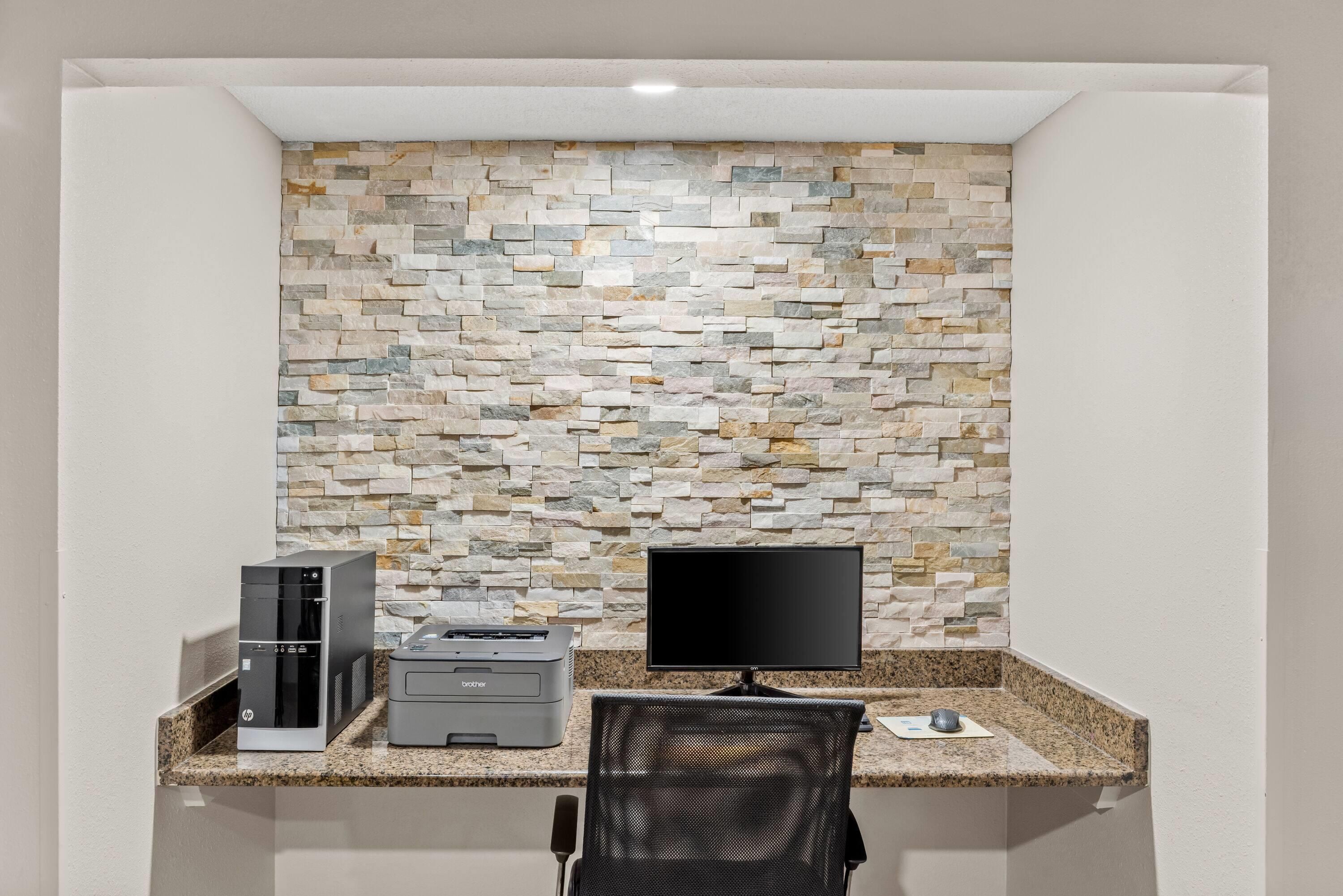 Un petit bureau avec un mur en pierre, un ordinateur de bureau, une imprimante et une chaise.