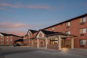 A brick building with a covered entrance and a car parked in front. - Days Inn & Suites by Wyndham Des Moines Airport (Des Moines)