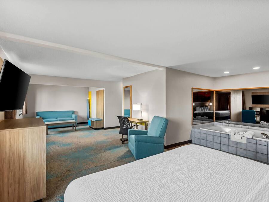 A hotel room with a bed, a desk, a chair, a TV, a sofa, and a bathroom with a bathtub and mirror.